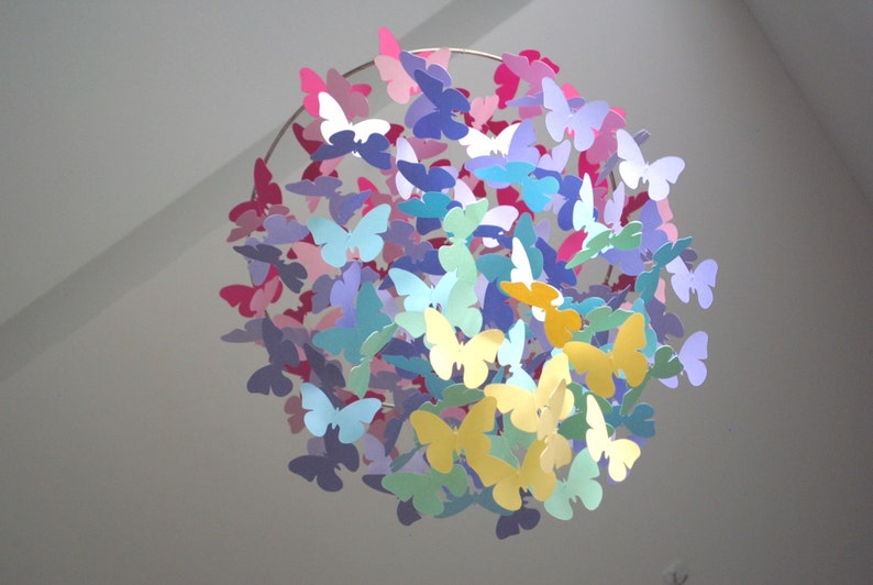 May include: A colorful paper butterfly mobile with butterflies in shades of pink, purple, blue, yellow, and green hanging from a circular metal frame.