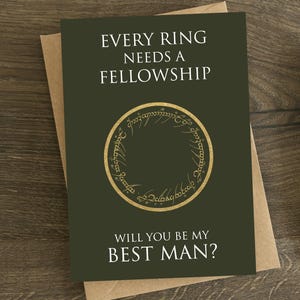 May include: A greeting card with the text "EVERY RING NEEDS A FELLOWSHIP" and "WILL YOU BE MY BEST MAN?" on a dark green background. The card features a gold ring design. The card is on a brown envelope, with a pen and stamp nearby.