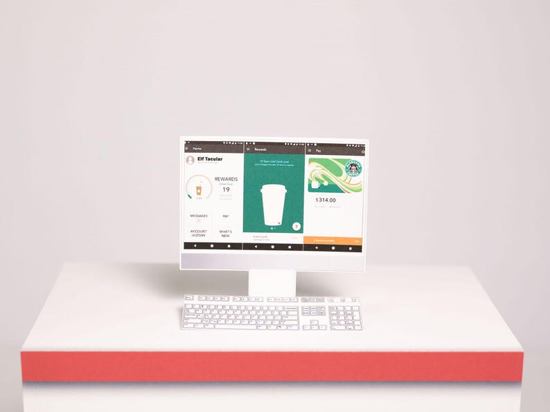 May include: A white computer monitor and keyboard display a mobile application interface with three panels. The screen shows a user profile named Elf Tacolar, a rewards section with a cup icon, and a payment card with a Starbucks logo and 1314.00.