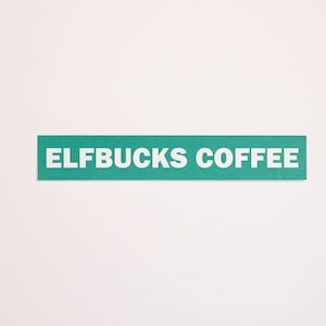 May include: A rectangular teal sticker featuring the white text ELFBUCKS COFFEE in a bold, sans-serif font. The sticker has a flat, matte finish and is presented against a plain, light-colored background, showcasing the clean, horizontal design.