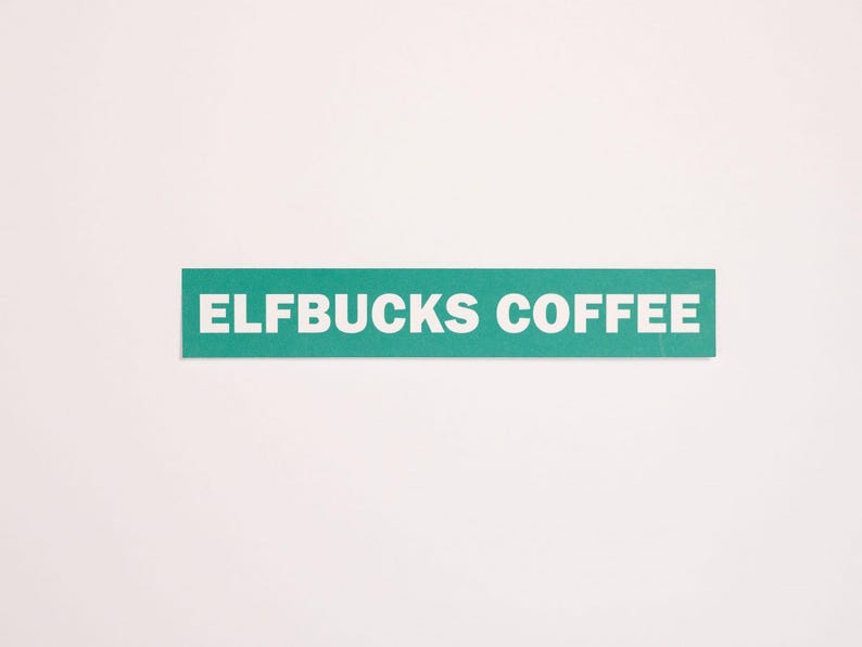 May include: A rectangular teal sticker featuring the white text ELFBUCKS COFFEE in a bold, sans-serif font. The sticker has a flat, matte finish and is presented against a plain, light-colored background, showcasing the clean, horizontal design.