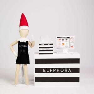 May include: An elf doll wearing a black apron with the text "ELFPHORA" stands next to a counter with the same text. A computer screen displays an online shopping interface. A shopping bag and a red and white hat complete the scene.