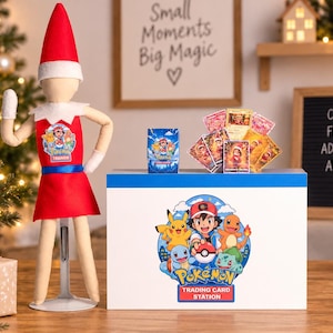 May include: A plush elf doll wearing a red hat and tunic with a Pokemon trainer emblem, standing next to a white box labeled Pokemon Trading Card Station. The box features a graphic of Ash Ketchum, Pikachu, and other Pokemon, with a deck of cards.
