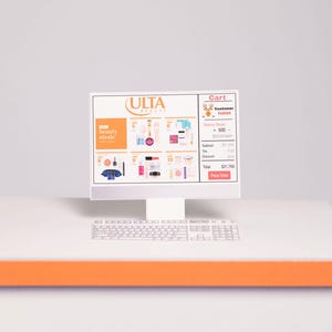 Puede incluir: Un monitor de computadora blanco que muestra un carrito de compras en l&iacute;nea de ULTA Beauty. La pantalla muestra varios productos de belleza y un resumen del carrito. Un teclado blanco est&aacute; debajo del monitor, y el escritorio tiene un acento naranja.