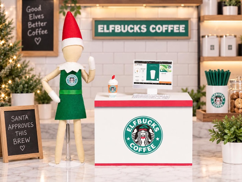 May include: A miniature elf doll wearing a green apron and red hat stands beside a white counter labeled Elfbucks Coffee. The counter features a computer monitor, a small coffee cup, and a logo with a siren graphic. A sign reads Santa Approves This Brew.