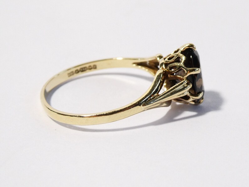 Op de afbeelding: Een gouden ring met een grote, ovale, donkerbruine edelsteen gezet in een delicate, sierlijke setting.