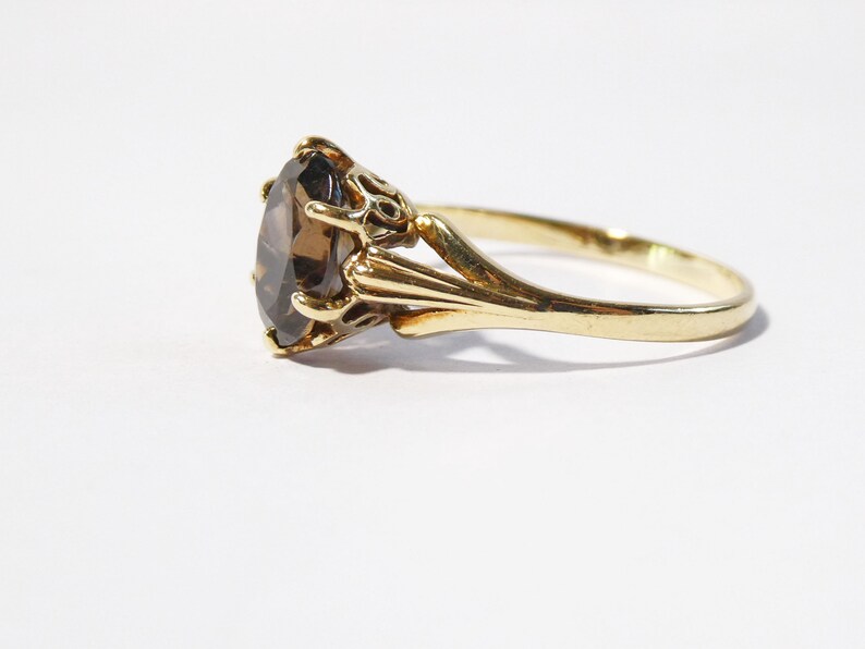 Op de afbeelding: Een gouden ring met een grote, ovale, bruine edelsteen gezet in een decoratieve, sierlijke zetting.