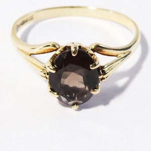 Op de afbeelding: Een gouden ring met een bruine ovale edelsteen in een kraalbezetting. De ring heeft een delicate, gebogen band.