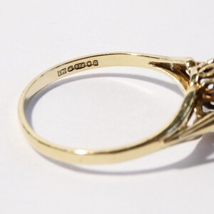 Op de afbeelding: Een gouden ring met een grote, donkerbruine edelsteen gezet in een delicaat, sierlijk ontwerp. De ring is gemarkeerd met "375" aan de binnenkant van de band.