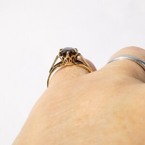 Op de afbeelding: Een gouden ring met een bruine edelsteen in een kroonvormige zetting.