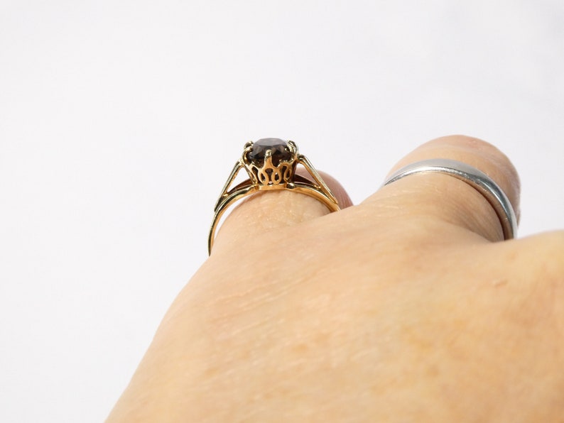 Op de afbeelding: Een gouden ring met een bruine edelsteen in een kroonvormige zetting.