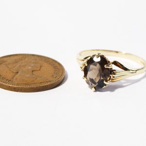 Op de afbeelding: Een gouden ring met een bruine ovale edelsteen. De ring is gezet met een delicaat, versierd ontwerp.