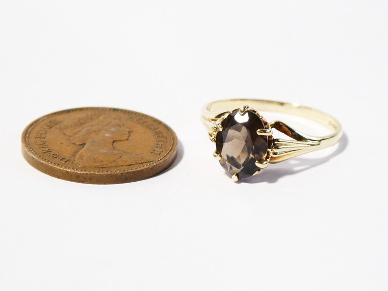 Op de afbeelding: Een gouden ring met een bruine ovale edelsteen. De ring is gezet met een delicaat, versierd ontwerp.