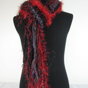 May include: A long, black and red scarf with a fluffy texture. The scarf is made of yarn and has a fringe at the bottom.