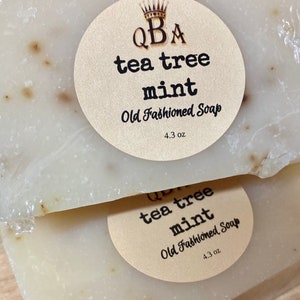 May include: Two bars of white soap with brown flecks. The soap is labeled "QBA tea tree mint Old Fashioned Soap 4.3 oz."