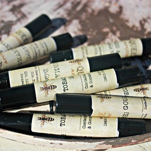 May include: A close-up of a collection of small, black, roll-on bottles with labels featuring a bee motif and text that includes "Solid & Coconut", "Tobacco", "Queen Bee", and "PEI GOU".