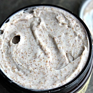 May include: A close-up of a white body scrub with brown sugar granules in a black jar.