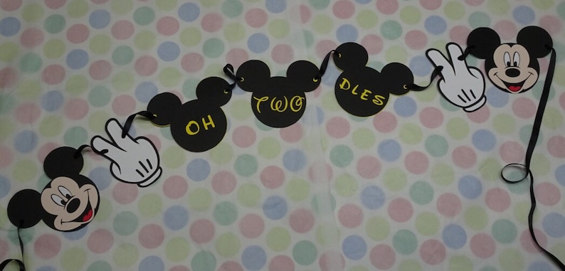 May include: A black Mickey Mouse-themed banner with the words "OH TWO DLES" in yellow. The banner includes Mickey Mouse heads and white gloved hands. The background is a polka dot pattern.
