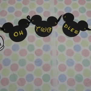 May include: A black banner with Mickey Mouse and white gloved hands. The banner reads "OH TWO DLES" in yellow lettering. The banner is strung with black ribbon and is on a polka dot background.