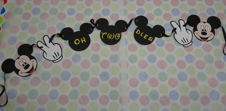 May include: A black banner with Mickey Mouse and white gloved hands. The banner reads "OH TWO DLES" in yellow lettering. The banner is strung with black ribbon and is on a polka dot background.