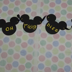 May include: A black Mickey Mouse-themed banner with the words "OH TWO DLES" in gold lettering. The banner includes Mickey Mouse heads and white gloved hands. The background is a polka dot pattern in various pastel colors.