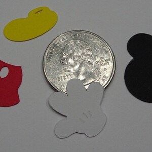 Puede incluir: Cinco recortes de papel de personajes de Mickey Mouse: pantalones rojos, sombrero amarillo, guante blanco y dos orejas negras. Los recortes est&aacute;n dispuestos sobre una superficie blanca junto a una moneda de veinticinco centavos de d&oacute;lar estadounidense para comparar el tama&ntilde;o.
