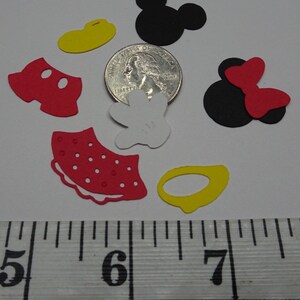 Puede incluir: Un conjunto de recortes de papel rojo, amarillo, negro y blanco de los personajes de Mickey Mouse y Minnie Mouse. Los recortes miden aproximadamente 2,5 cm y est&aacute;n dispuestos sobre una superficie blanca junto a una regla.