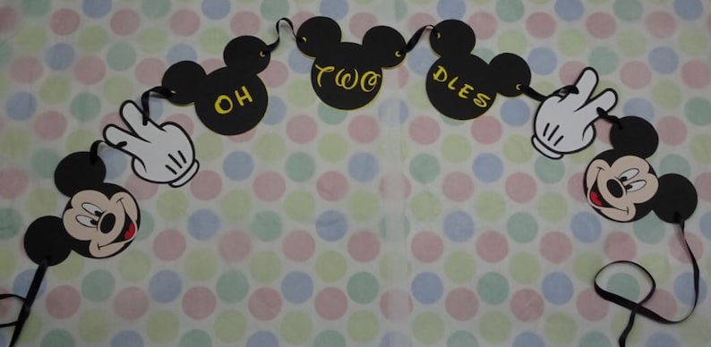 May include: A black Mickey Mouse-themed banner with the words "OH TWO DLES" in yellow. The banner includes Mickey Mouse heads, white gloved hands, and a smiling Mickey Mouse face. The banner is on a polka dot background.