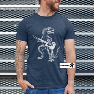 May include: A navy blue t-shirt with a white graphic of a dinosaur playing a guitar. The t-shirt has the text "SEEMBO" on the bottom right corner.