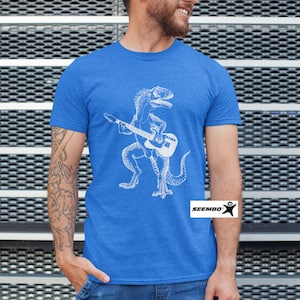 May include: A royal blue t-shirt with a white graphic of a dinosaur playing a guitar. The dinosaur is standing on its hind legs and holding a guitar in its front paws. The t-shirt has the word "SEEMBO" printed on the bottom right corner.