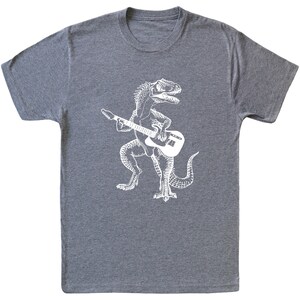 May include: A heather grey t-shirt with a white graphic of a dinosaur playing an electric guitar.
