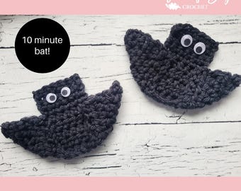 May include: Two dark gray crochet bats with googly eyes are displayed on a white wooden surface. One bat is in the foreground, and the other is in the background. A black circle with the text "10 minute bat!" is in the upper left corner.