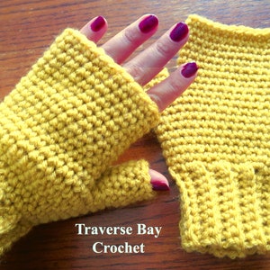 May include: Mustard yellow crochet fingerless gloves. The gloves are handmade with a textured stitch pattern. The text "Traverse Bay Crochet" is visible at the bottom of the image.