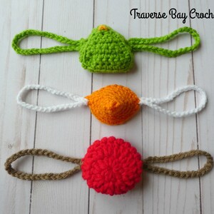 May include: Three crocheted items in green, orange, and red, each with a loop. The green item has a small yellow accent. The text "Traverse Bay Crochet" is in the upper right corner.