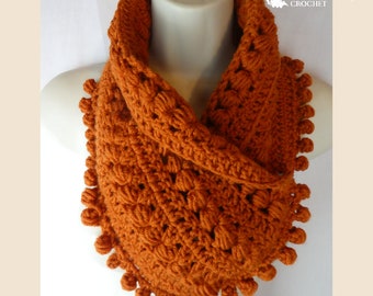 May include: An orange crochet infinity scarf with a textured, bobble stitch design. The scarf has a decorative edge of small, round bobbles. The text "Traverse Bay Crochet" is visible in the upper right corner.