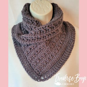 Pode incluir: Cachecol de gola de crochê cinza escuro, exibido em uma cabeça de manequim. O cachecol tem um padrão de ponto texturizado e um design vazado decorativo na borda inferior. O texto "Traverse Bay Crochet" é visível no canto inferior direito.