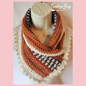 May include: A handmade crochet cowl scarf in shades of orange, brown, and cream. The scarf features a textured stitch pattern and a scalloped edge. The text "Traverse Bay Crochet" is visible in the upper right corner.