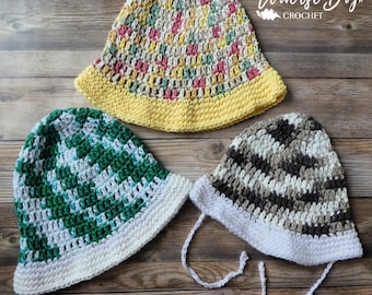 May include: Three handmade crochet hats in various colors. One hat is yellow with a multi-colored top, another is green and white, and the third is brown and white with white ties. The hats are displayed on a wooden surface. The text "Traverse Bayx Crochet" is visible.