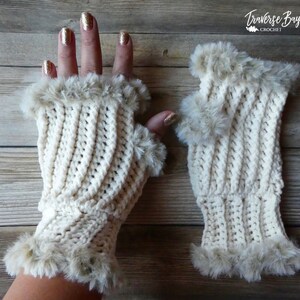 May include: Cream-colored, fingerless crochet gloves with a ribbed design and faux fur trim. The gloves are displayed on a wooden surface. The gloves are handmade and feature a soft, textured appearance. The design includes a cuff and wrist warmer.