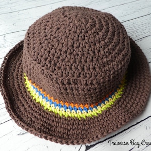 May include: A brown crochet hat with a wide brim. The hat features a colorful band with orange, yellow, blue, and green stripes. The hat is handmade and suitable for sun protection.