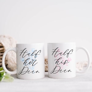 May include: Two white ceramic mugs with black calligraphy that reads "Half her Deen" and "Half his Deen". The mug with "her" has a blue floral design and the mug with "his" has a pink floral design.