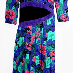 May include: A vintage floral dress with a vibrant pattern of pink, teal, and blue flowers on a black background. The dress features a black waist panel with purple trim and three-quarter sleeves. The dress is displayed on a mannequin.