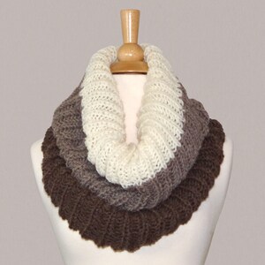 May include: A brown, grey, and white knitted infinity scarf. The scarf is made from a soft, chunky yarn and is ideal for keeping warm in the winter.