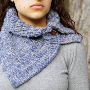 Peut inclure: Un col en tricot bleu et gris avec un bouton en bois. Le col est porté par une personne aux cheveux longs et bruns.