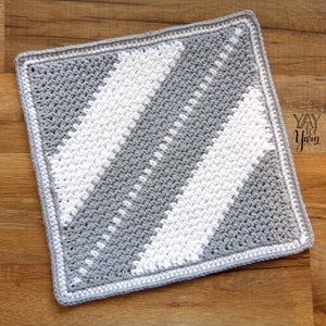 May include: A gray and white crocheted square with a diagonal stripe pattern. The square has a white border.