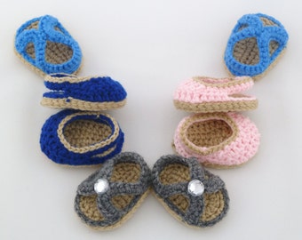 Op de afbeelding: Zes paar gehaakte babysandalen in blauw, roze en grijs. De sandalen hebben een bandje over de bovenkant en een gespsluiting. Sommige sandalen hebben een strass-versiering.