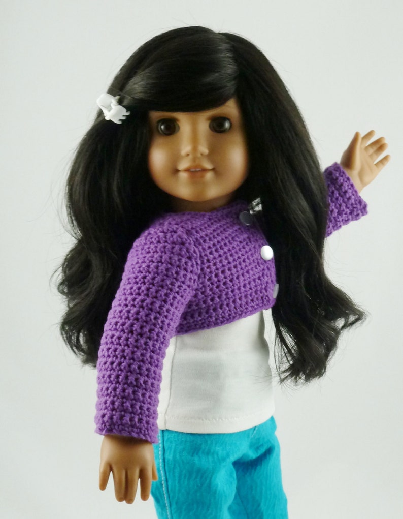 K&ouml;nnte beinhalten: Eine Puppe mit langen schwarzen Haaren, die eine lila geh&auml;kelte Strickjacke, ein wei&szlig;es T-Shirt und eine blaue Jeans tr&auml;gt.