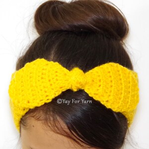 May include: A yellow crocheted headband with a bow. The headband is worn by a person with brown hair in a bun.
