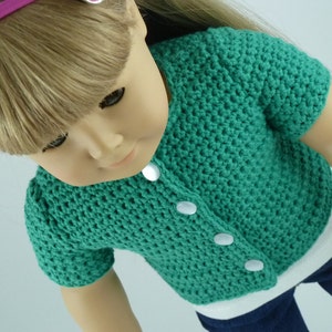 K&ouml;nnte beinhalten: Eine gr&uuml;ne geh&auml;kelte Strickjacke mit wei&szlig;en Kn&ouml;pfen. Die Strickjacke hat kurze &Auml;rmel und einen runden Ausschnitt.
