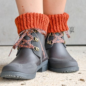 May include: A pair of black rain boots with brown and black leopard print laces. The boots have a brown knitted cuff around the top.